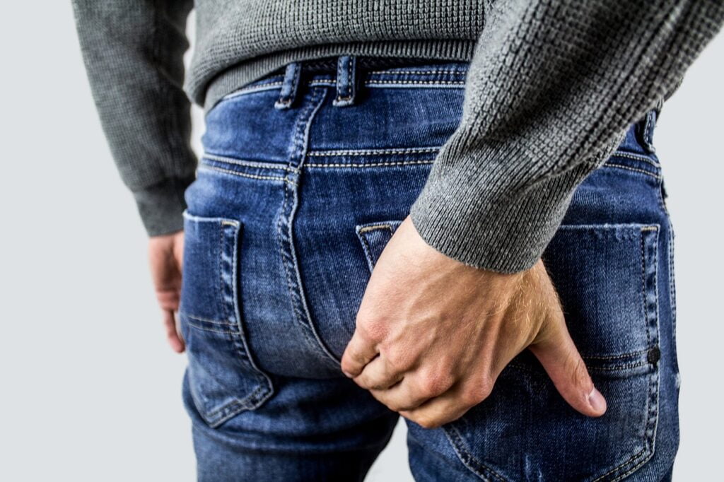 Male holding his bottom with his right hand signalling issues with hemorrhoids and how to shrink them naturally.