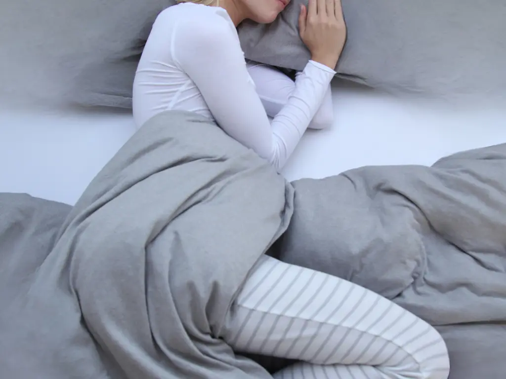 woman sleeping on her left side with her knees slightly towards her chest demonstrating the best sleeping position for people with hemorrhoids