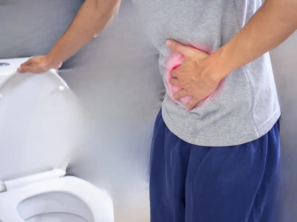 Man holding onto a toilet seat while holding his stomach signalling pain from constipation and hemorrhoids